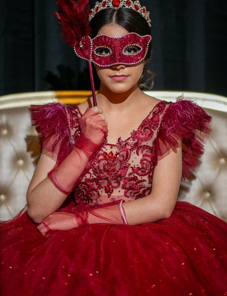 Young woman in a red masquerade mask and ornate red gown posing.