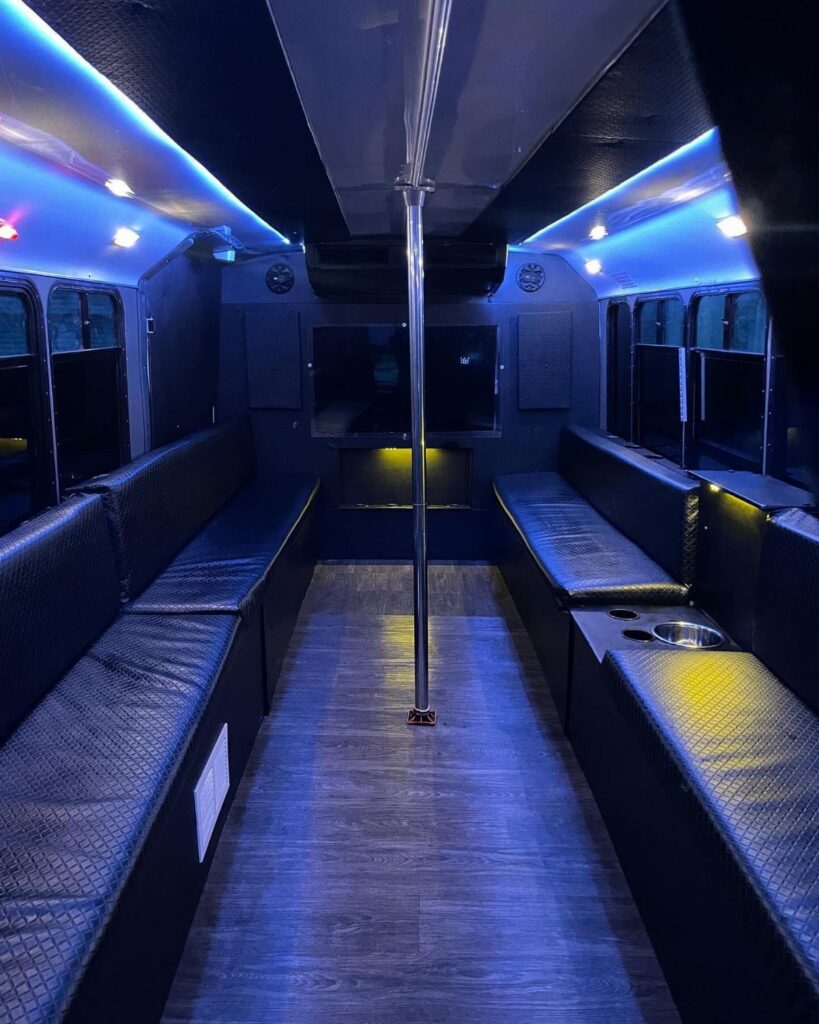 Interior of a party bus with black leather seats and blue neon lighting.