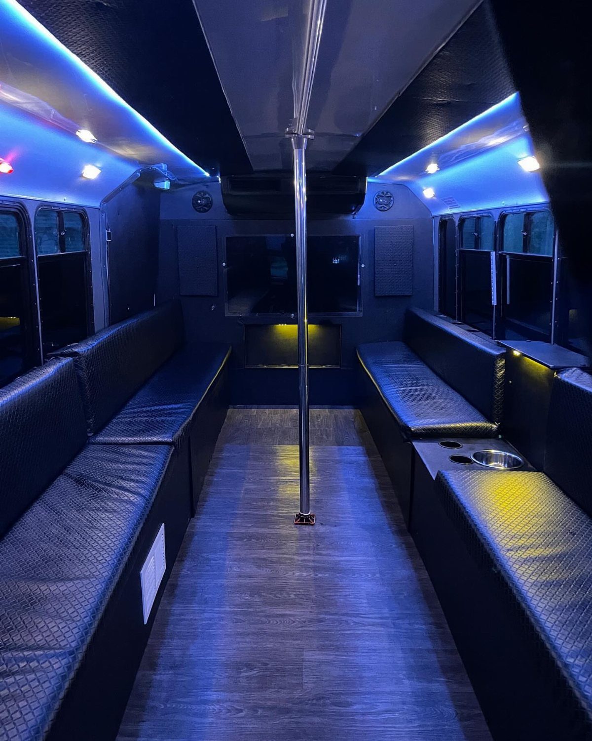 Interior of a party bus with black leather seats and blue neon lighting.