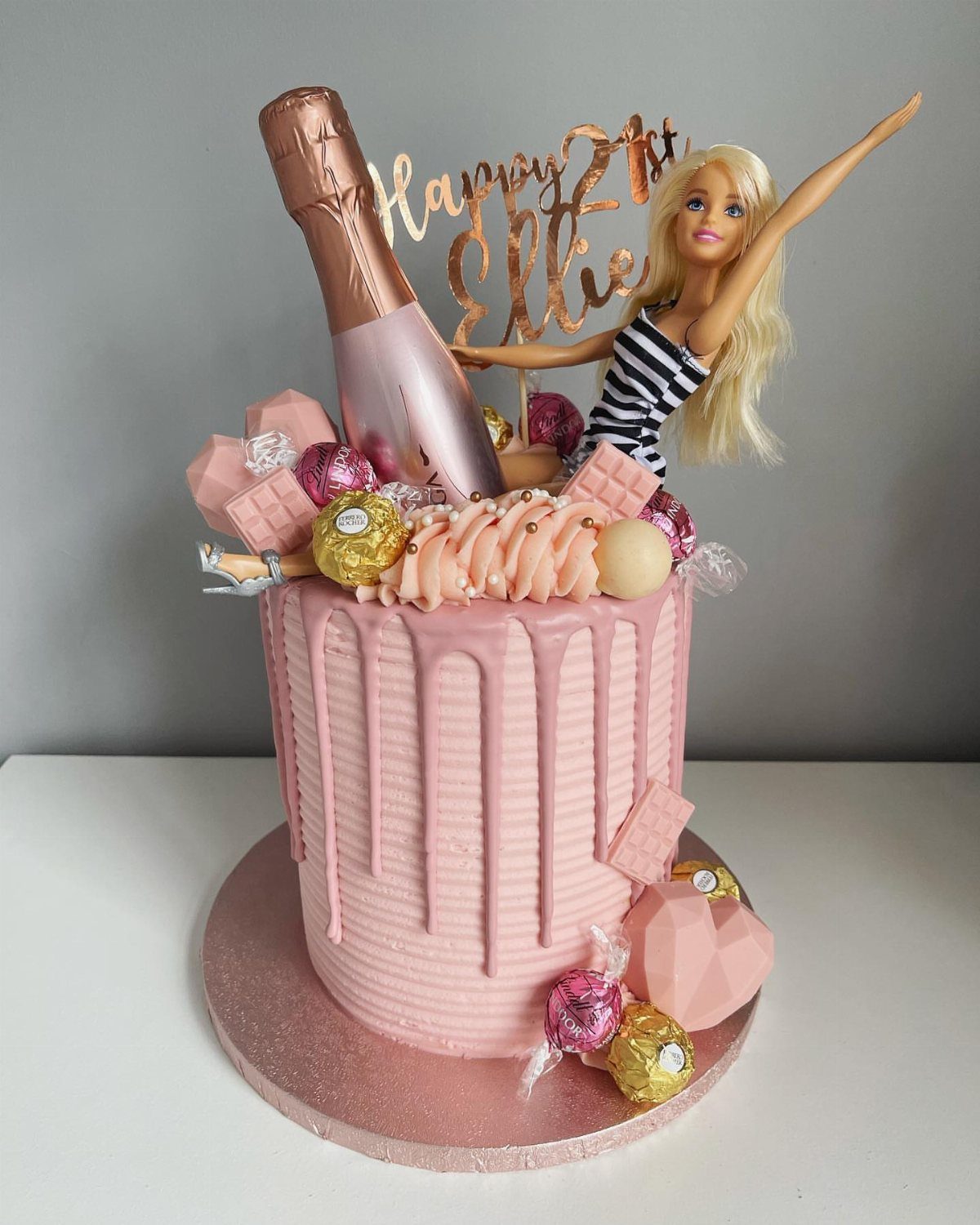 Pink birthday cake topped with a Barbie doll and a champagne bottle.
