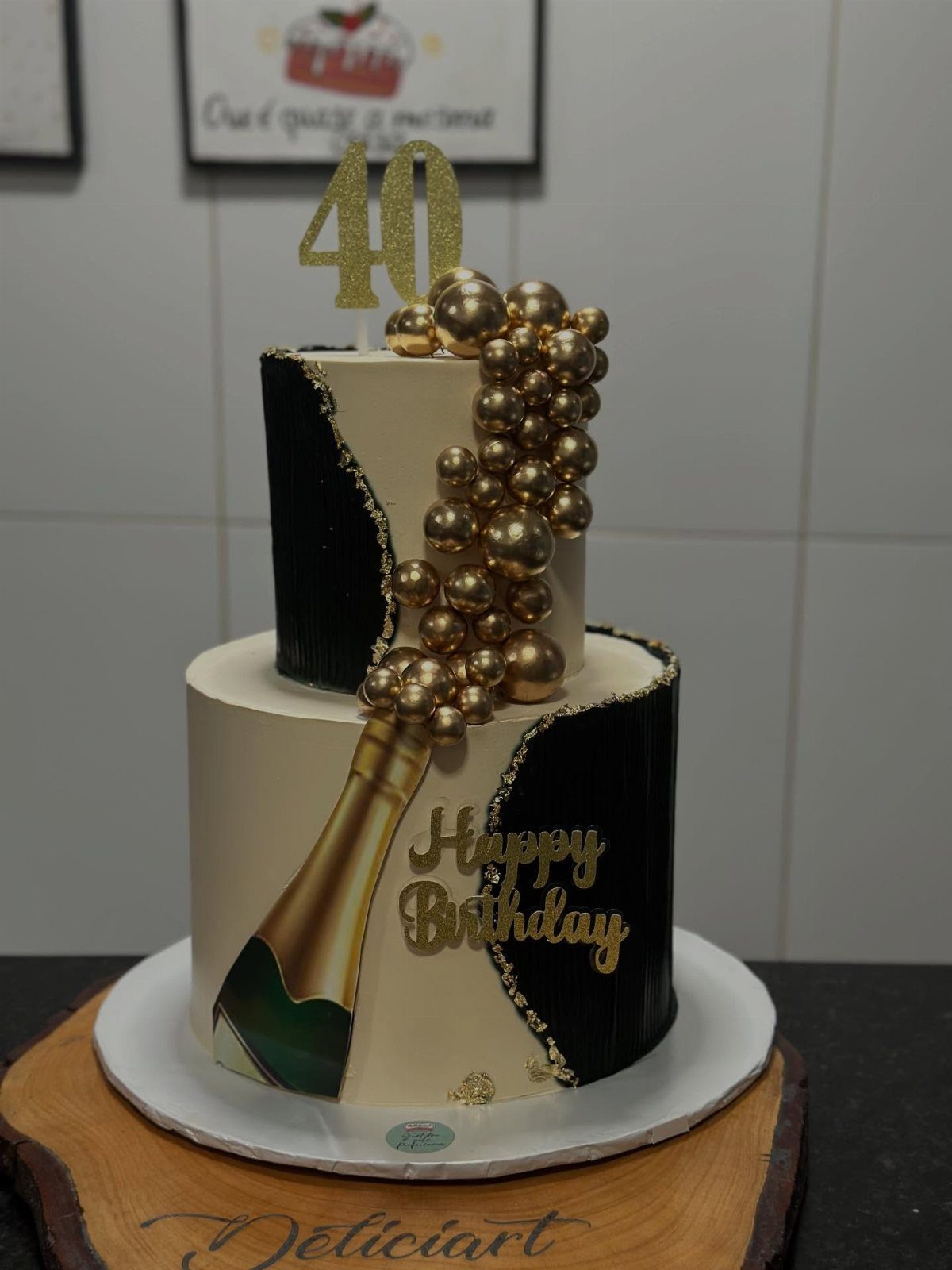 Two-tier white and black birthday cake with gold champagne bottle and 40 topper