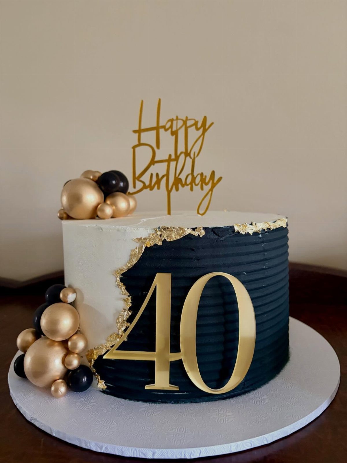 Black and white birthday cake with gold 40 topper and gold spheres.