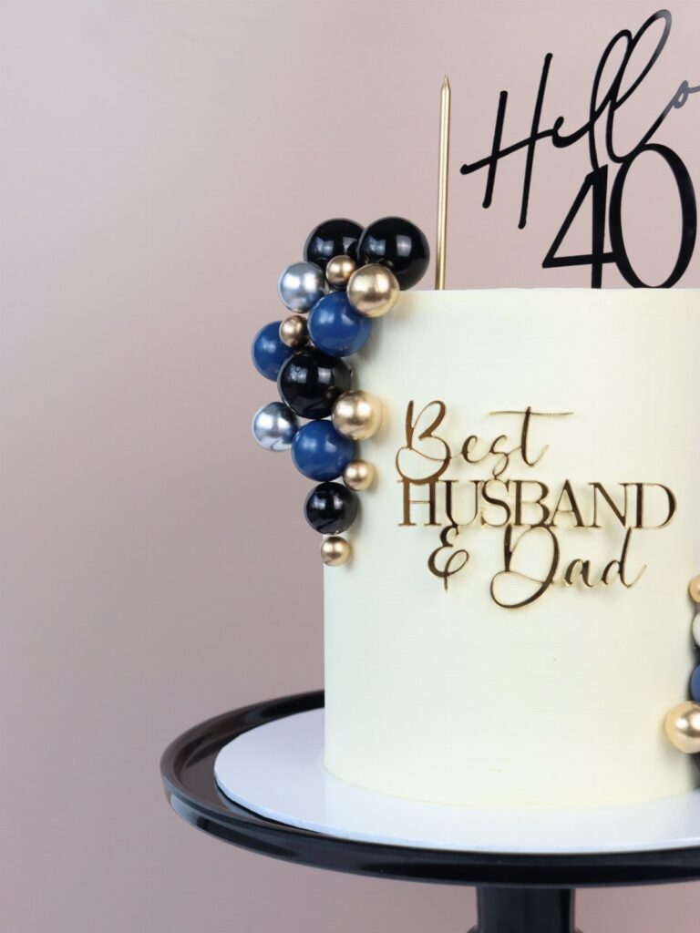 White birthday cake with blue and gold spheres and Best Husband & Dad topper