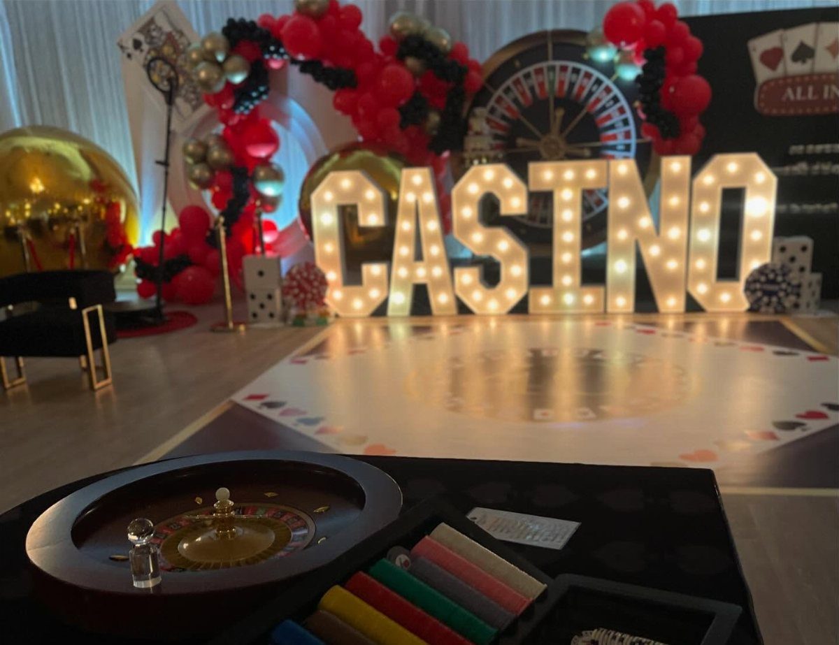 Casino party setup with large glowing letters, red balloons, and gaming equipment.