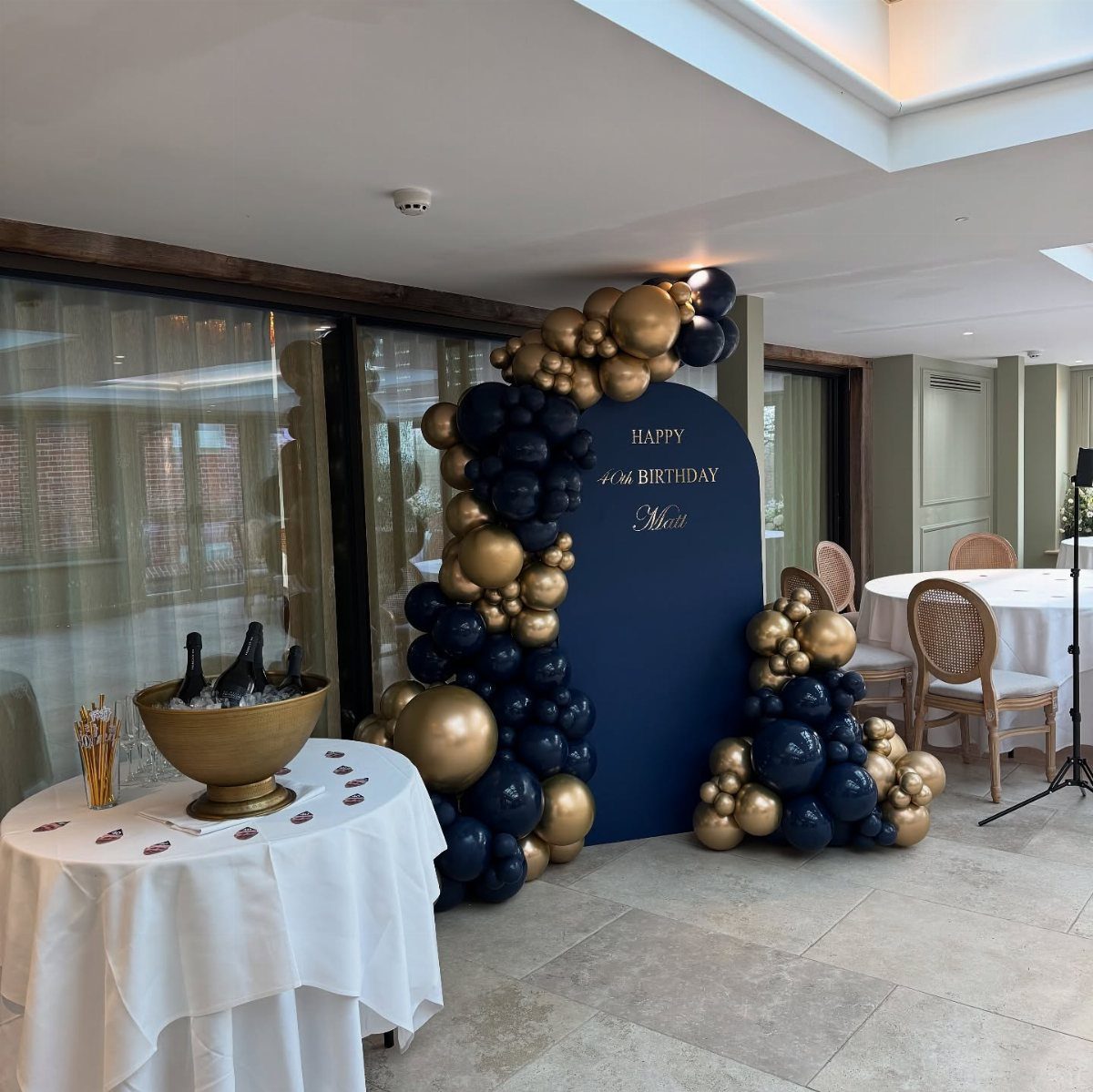 Navy blue and gold balloon arch with a birthday backdrop and champagne table.