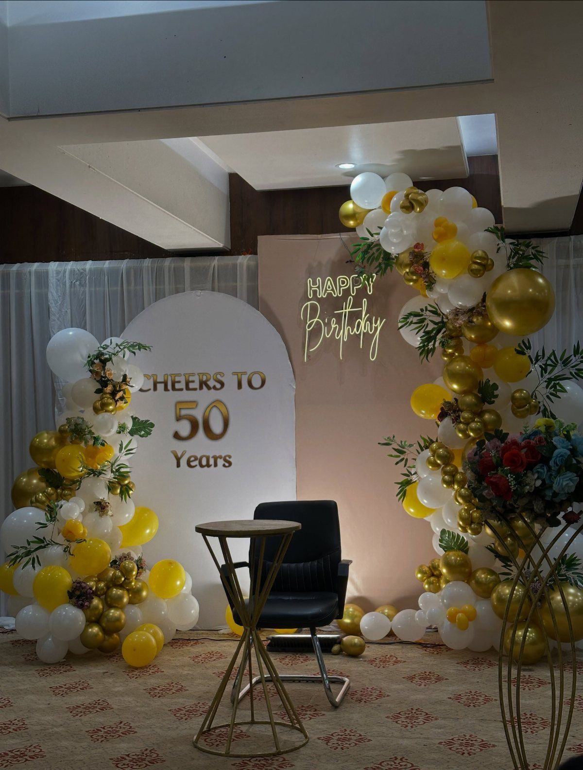Gold and white balloon arch surrounding a 50th birthday backdrop and seating area.