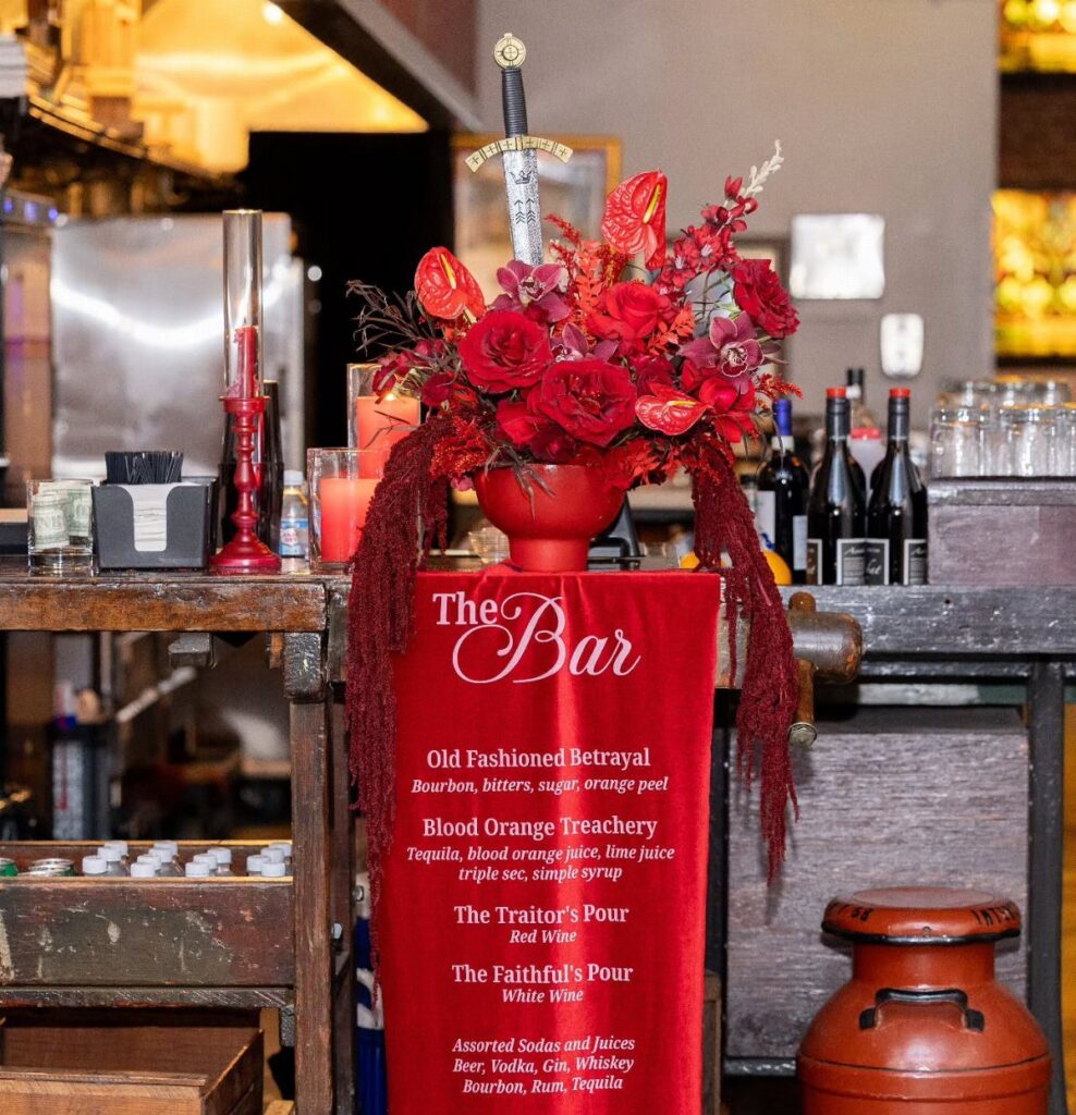 Themed bar setup with red flowers, a sword, and a betrayal-themed cocktail menu.