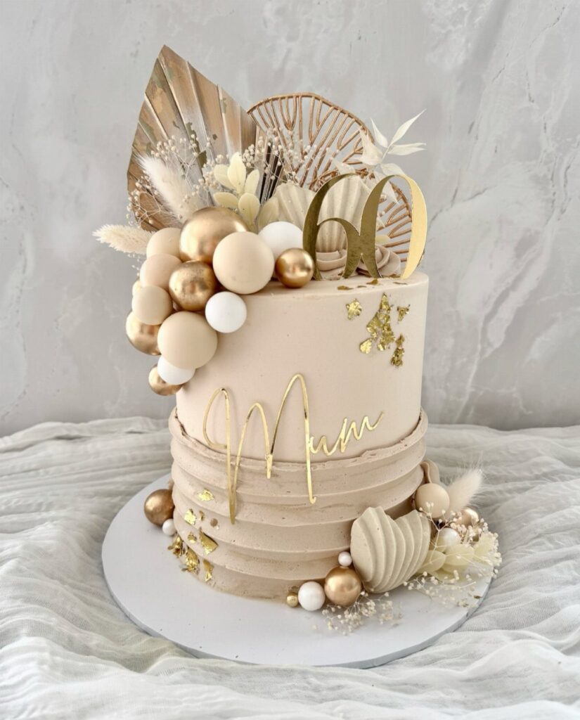 Beige birthday cake with gold 60 and Mum toppers, spheres, and dried leaves.