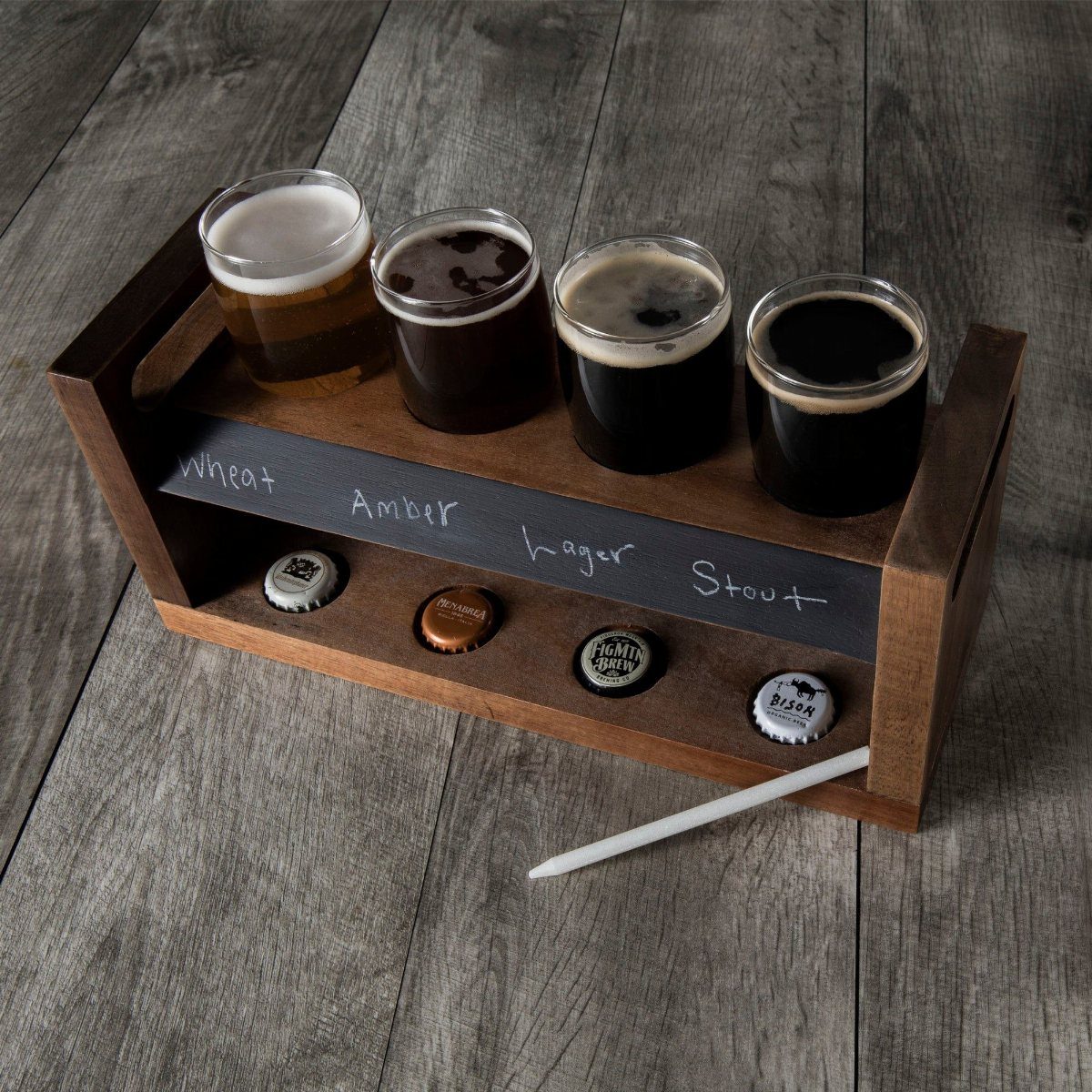Beer flight station with four tasting glasses in a wooden holder on wood.