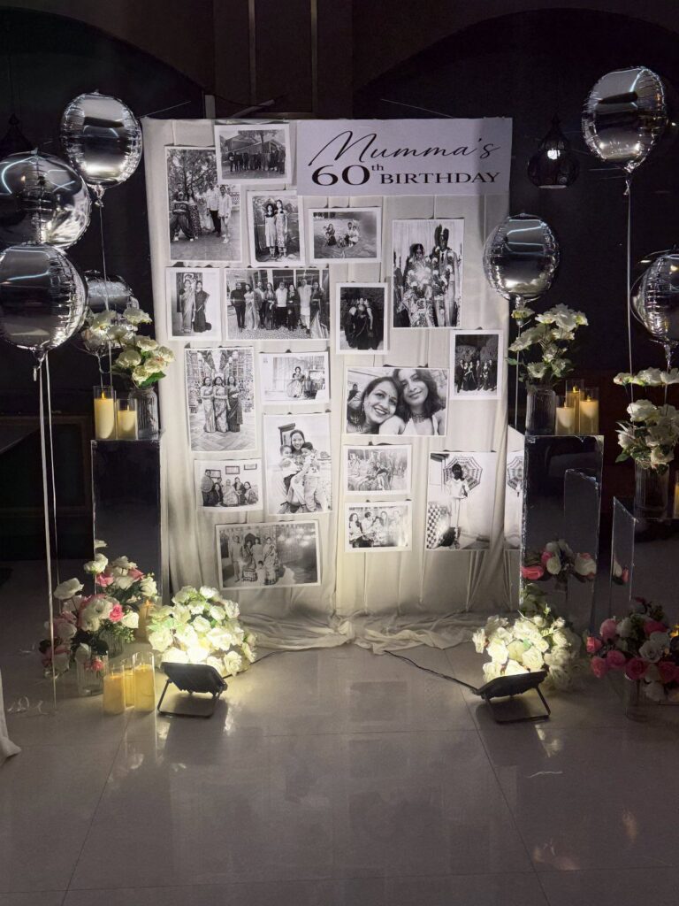 Birthday photo wall for a 60th celebration with silver balloons and white flowers