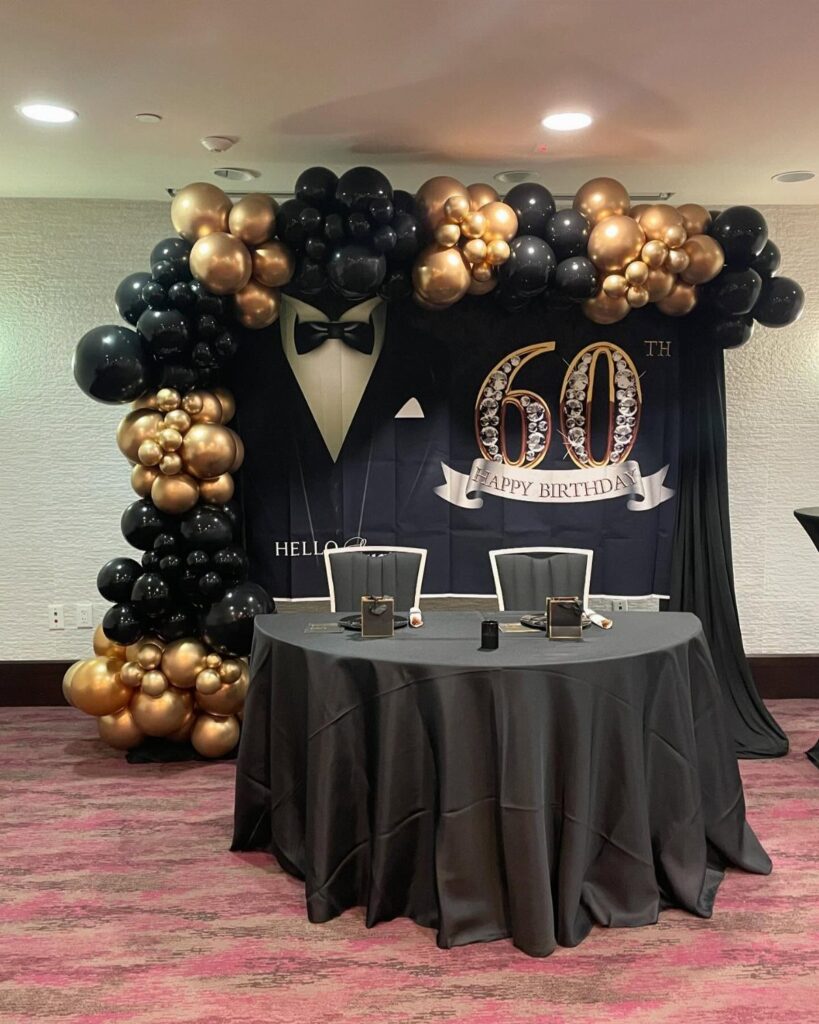 Tuxedo themed 60th birthday party setup with black and gold balloon arch.