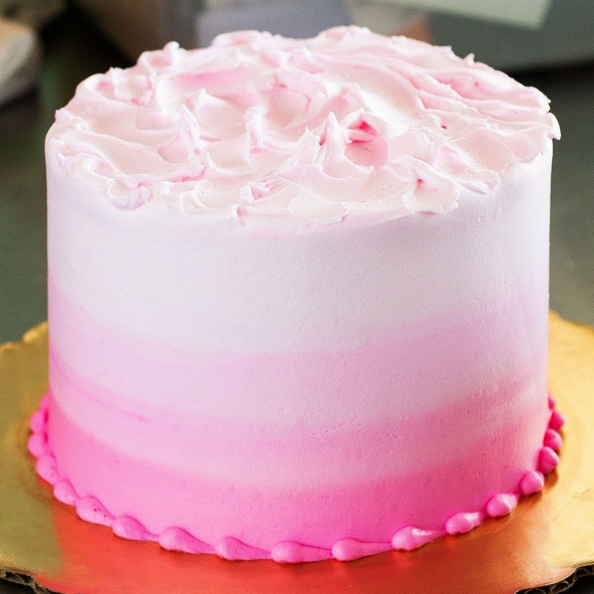 Pink and white ombre frosted cake with swirls on top and gold base.