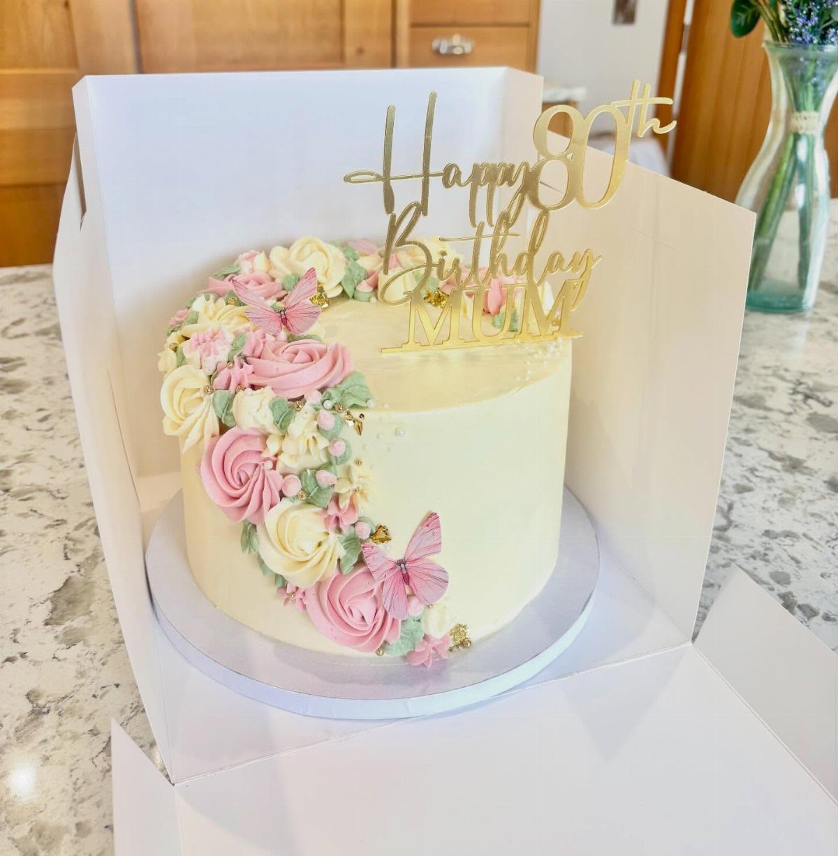 White birthday cake with pink roses, butterflies, and a gold 80th birthday topper.