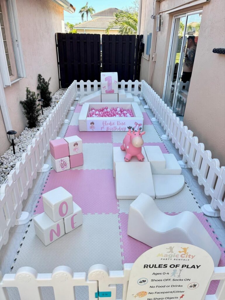 Baby party setup with pink foam mats, ball pit, and white picket fence.