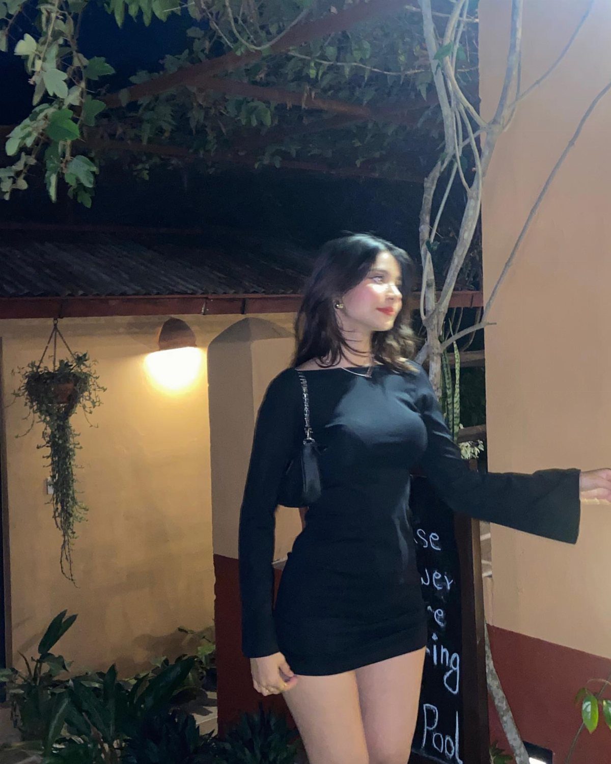 Woman in a short black long-sleeved dress posing outdoors at night.