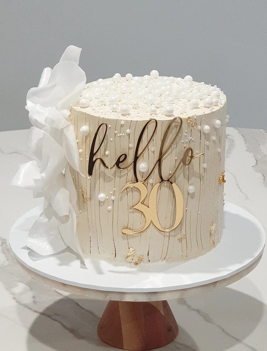 Cream-colored birthday cake with gold hello 30 topper and white pearl decorations