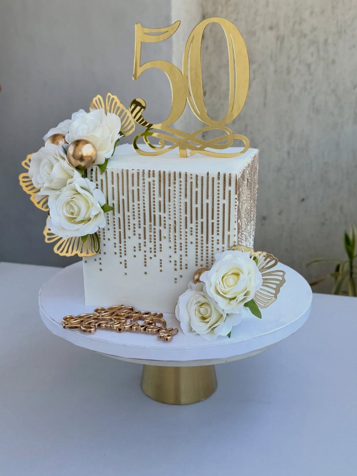 White birthday cake with gold accents, white roses, and a gold 50 topper.
