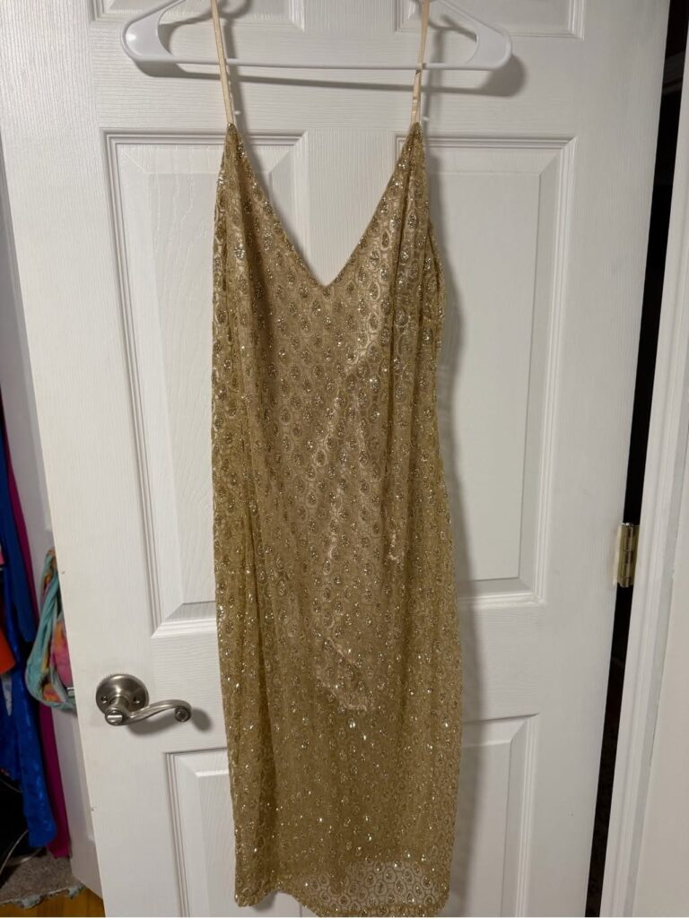 Gold sequined midi dress with thin straps hanging on a white door.
