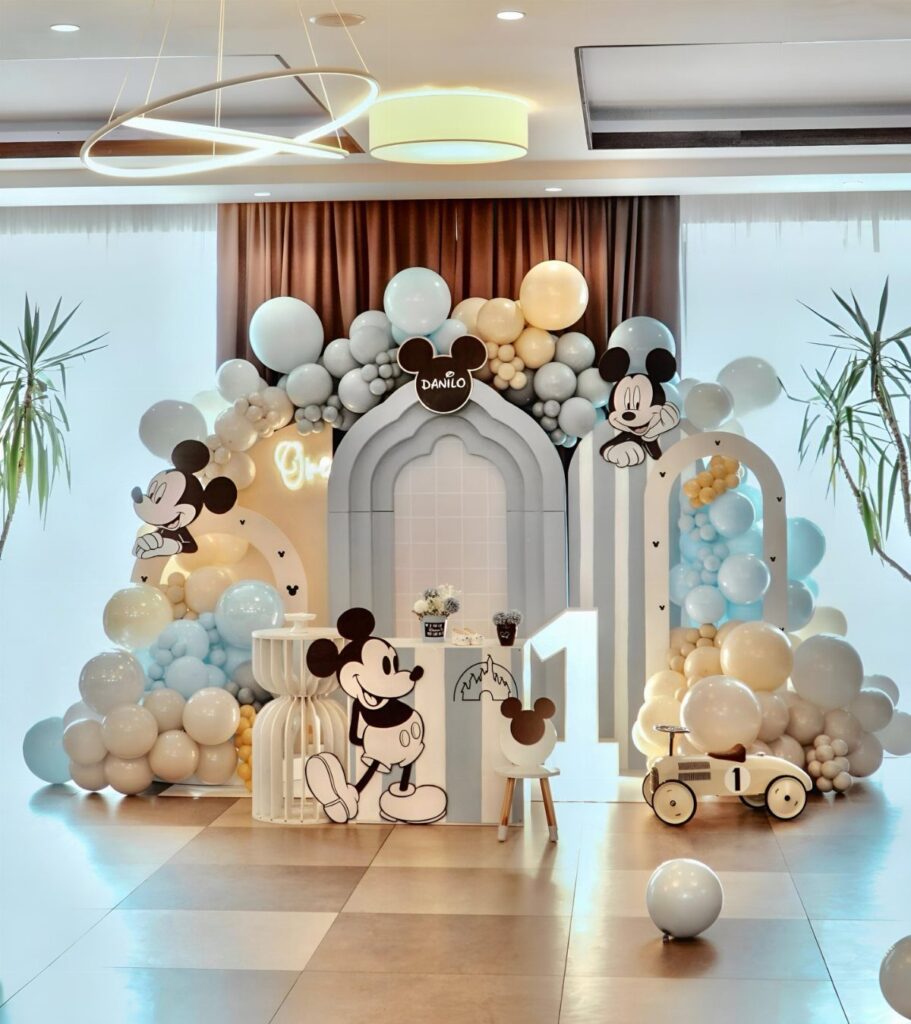 Mickey Mouse birthday party decoration with blue and white balloons and character cutouts.