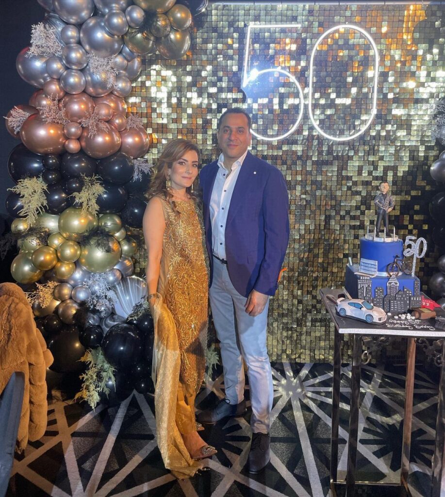 Couple posing at a 50th birthday party with gold balloons and neon sign.
