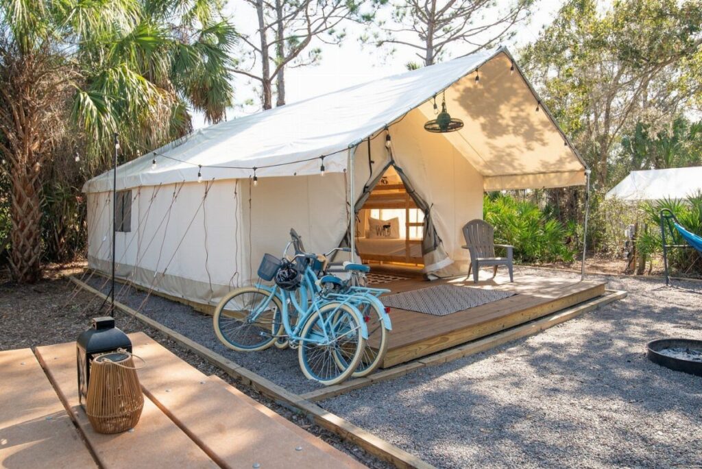 White canvas glamping tent on a wooden deck with two blue bicycles outside.
