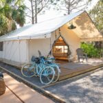White canvas glamping tent on a wooden deck with two blue bicycles outside.