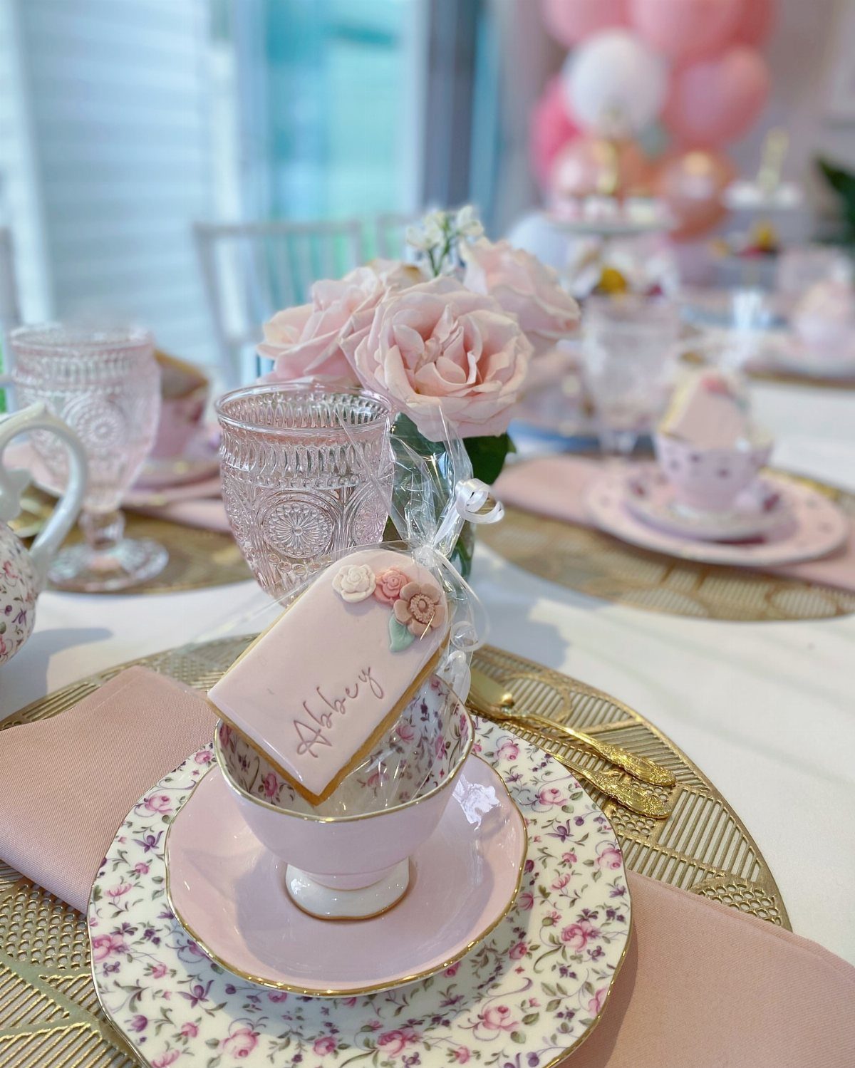 Pink teacup and saucer with a personalized cookie and roses at a tea party.