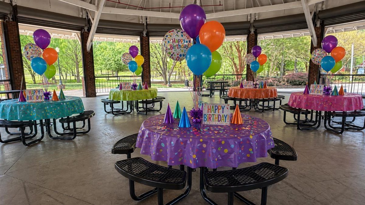 Colorful birthday party table setups with balloons in a covered outdoor pavilion.